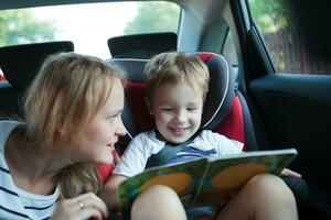 Garoto segurando livro sentado dentro uma carro com mãe foto