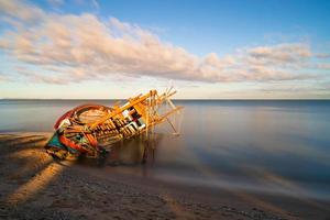 barco de pesca danificado na praia ao nascer do sol foto