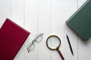 conceito de educação, livro, caneta, óculos, lupa em fundo branco de madeira foto