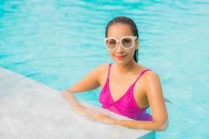 retrato bela jovem asiática relaxando sorriso ao redor de uma piscina externa em hotel resort foto