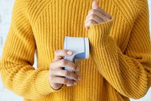 mulher dentro amarelo suéter usando tecido pílulas removendo ferramenta foto
