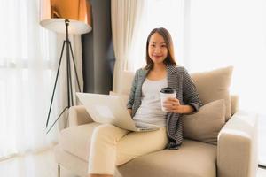lindo jovem retrato asiático usando computador e laptop com uma xícara de café sentado no sofá foto