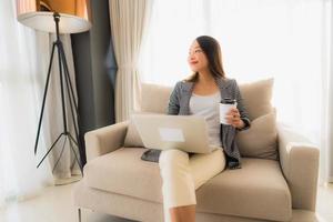 lindo jovem retrato asiático usando computador e laptop com uma xícara de café sentado no sofá foto