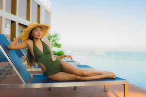 lindas jovens mulheres asiáticas sorriso feliz relaxando ao redor da piscina ao ar livre em hotel resort para viagens de férias foto