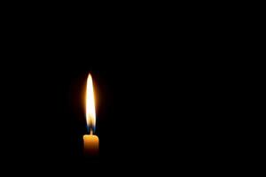 solteiro queimando vela chama ou luz brilhando em uma pequeno amarelo vela em Preto ou Sombrio fundo em mesa dentro Igreja para Natal, velório ou memorial serviço com cópia de espaço foto