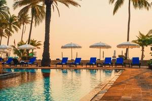 bela palmeira com piscina com cadeira de guarda-chuva em hotel resort de luxo na hora do nascer do sol - conceito de férias e férias foto