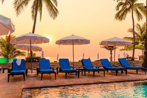 bela palmeira com piscina com cadeira de guarda-chuva em hotel resort de luxo na hora do nascer do sol - conceito de férias e férias