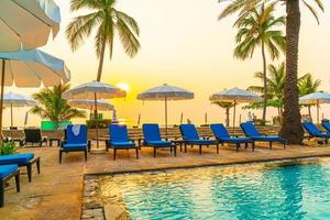 bela palmeira com piscina com cadeira de guarda-chuva em hotel resort de luxo na hora do nascer do sol - conceito de férias e férias foto