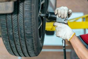 carro serviço, manutenção e pessoas conceito - auto mecânico homem com elétrico Chave de fenda mudando pneu às auto reparar serviço Centro foto