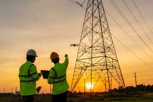 equipe trabalhos do engenheiros localização Socorro técnico usar zangão para vôo inspecionar equipamento em vez de do trabalhadores às a Alto Voltagem elétrico transmissão torre, elétrico poder estação foto