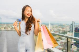 retrato linda jovem asiática feliz e sorrindo com cartão de crédito para sacola de compras da loja de departamentos foto