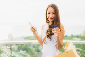 retrato linda jovem asiática feliz e sorrindo com cartão de crédito e celular ou telefone inteligente e sacola de compras foto