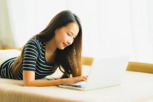 retrato bela jovem asiática usando computador notebook ou laptop no sofá na sala de estar foto