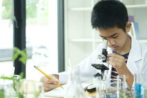 jovem cientista elementar estudante explora com microscópio foto