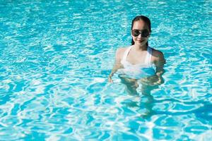 bela jovem asiática feliz e sorrindo na piscina para relaxar, viagens e férias foto