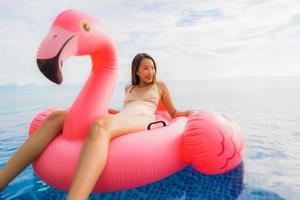 jovem mulher asiática em um flamingo flutuante inflável ao redor de uma piscina externa em um resort de hotel foto