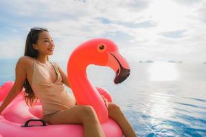 jovem mulher asiática em um flamingo flutuante inflável ao redor de uma piscina externa em um resort de hotel foto