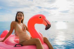 jovem mulher asiática em um flamingo flutuante inflável ao redor de uma piscina externa em um resort de hotel foto