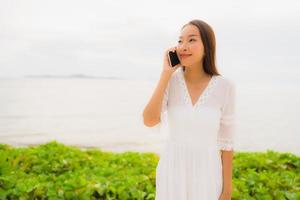 retrato de uma linda mulher asiática usar chapéu com um sorriso feliz por falar de telefone celular na praia foto