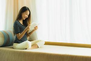 retrato de uma bela jovem asiática lendo um livro no sofá na sala de estar foto