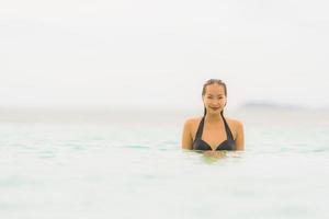 retrato bela jovem asiática usar biquíni ao redor da piscina em hotel resort perto do mar oceano praia foto