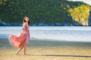 retrato jovem linda mulher asiática andar sorrindo e feliz na praia, mar e oceano foto