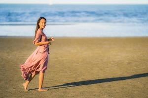 retrato jovem linda mulher asiática andar sorrindo e feliz na praia, mar e oceano foto