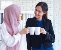 mulheres muçulmanas e amigas estrangeiras conversam e se cumprimentam no escritório moderno, as duas mulheres seguram a xícara de café branca, conceito de trabalho profissional e feliz