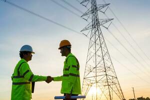 equipe trabalhos do engenheiros e técnico aperto de mão depois de trabalhos inspeções às a elétrico poder estação para Visão a planejamento trabalhos de produzindo eletricidade Alto Voltagem elétrico transmissão torre foto