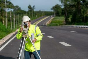 ásia agrimensor engenheiro trabalhador fazer medindo com teodolito em estrada funciona. pesquisa engenheiro às estrada construção site, agrimensor equipamento. foto