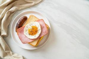 pão caseiro queijo torrado, presunto com cobertura e ovo frito com linguiça de porco no café da manhã foto