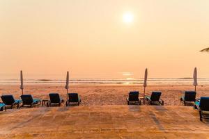 cadeira de praia guarda-sol com palmeira e praia do mar na hora do nascer do sol - conceito de férias e feriados foto