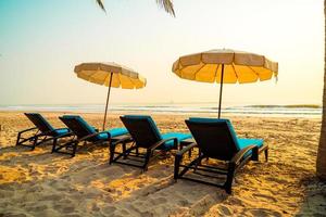 cadeira de praia guarda-sol com palmeira e praia do mar na hora do nascer do sol - conceito de férias e feriados