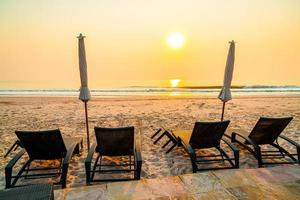 cadeira de praia guarda-sol com palmeira e praia do mar na hora do nascer do sol - conceito de férias e feriados