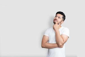 homem bonito asiático em uma camiseta branca pensando enquanto olha para cima sobre um fundo branco isolado foto