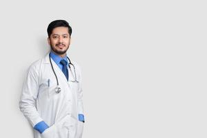 jovem médico masculino sorrindo com estetoscópio e o braço nos bolsos isolados no fundo branco. conceito de seguro saúde. foto