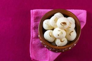 doce indiano - rasgulla, famoso doce bengali em tigela de barro com guardanapo no fundo rosa foto