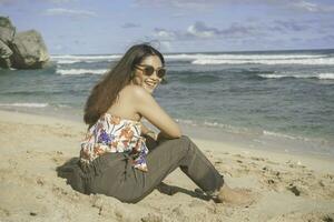 jovem ásia mulher sentar em a de praia areia. retrato sexy ásia senhora viajando e relaxante dentro a verão com tropical natureza. foto