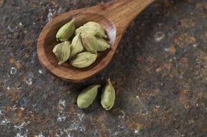 cápsulas de cardamomo em colher de pau em um plano de fundo texturizado foto