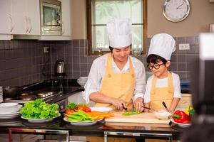 mulher asiática com filho cozinhando comida na cozinha de casa foto