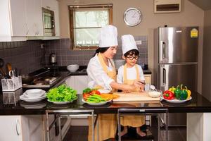 mulher asiática com filho cozinhando comida na cozinha de casa foto