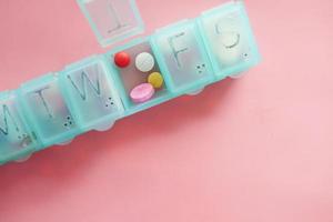 comprimidos médicos e cápsulas em uma caixa de comprimidos em fundo rosa foto