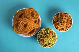 lanche indiano chakli, chakali ou murukku e besan grama farinha sev e chivada ou chiwada sobre fundo azul. comida diwali foto