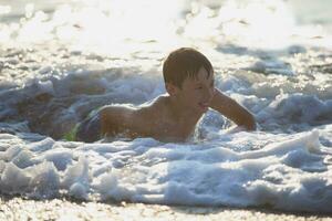 feliz adolescente Garoto tocam com mar ondas. a Garoto nada dentro a mar. foto