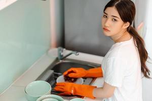 a mulher asiática está lavando pratos com um humor cansado foto