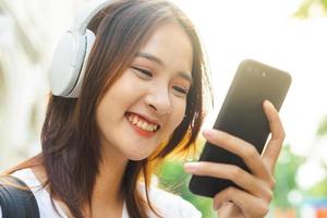 jovem asiática lendo texto em seu telefone e usando fones de ouvido para ouvir música na rua