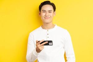 empresário asiático segurando o telefone para assistir a um filme sobre fundo amarelo foto
