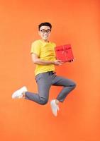homem asiático com camiseta amarela pulando no fundo laranja