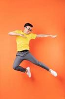 homem asiático com camiseta amarela pulando no fundo laranja