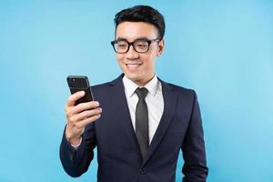Buisnessman asiático vestindo terno segurando smartphone sobre fundo azul